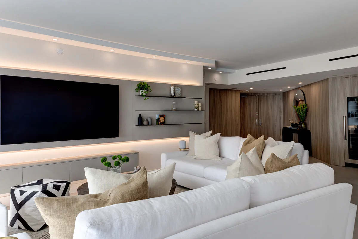 Great room with white sectional, backlit media wall and floating shelves